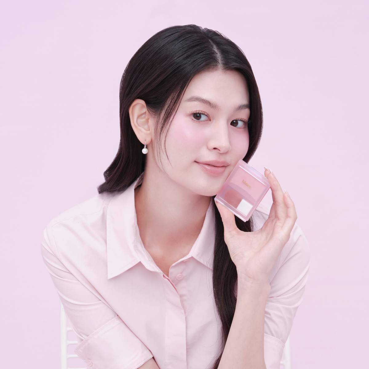 Hince Hug Layer Cheek Blush in a soft pink shade, displayed on a reflective surface with blush applicator brush nearby.