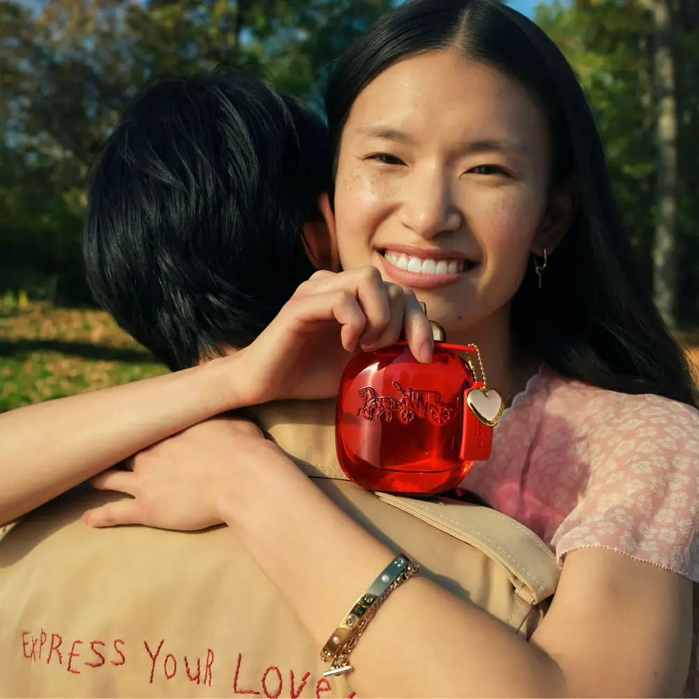 Female model hugging another model with a bottle of Coach Love perfume in her hand